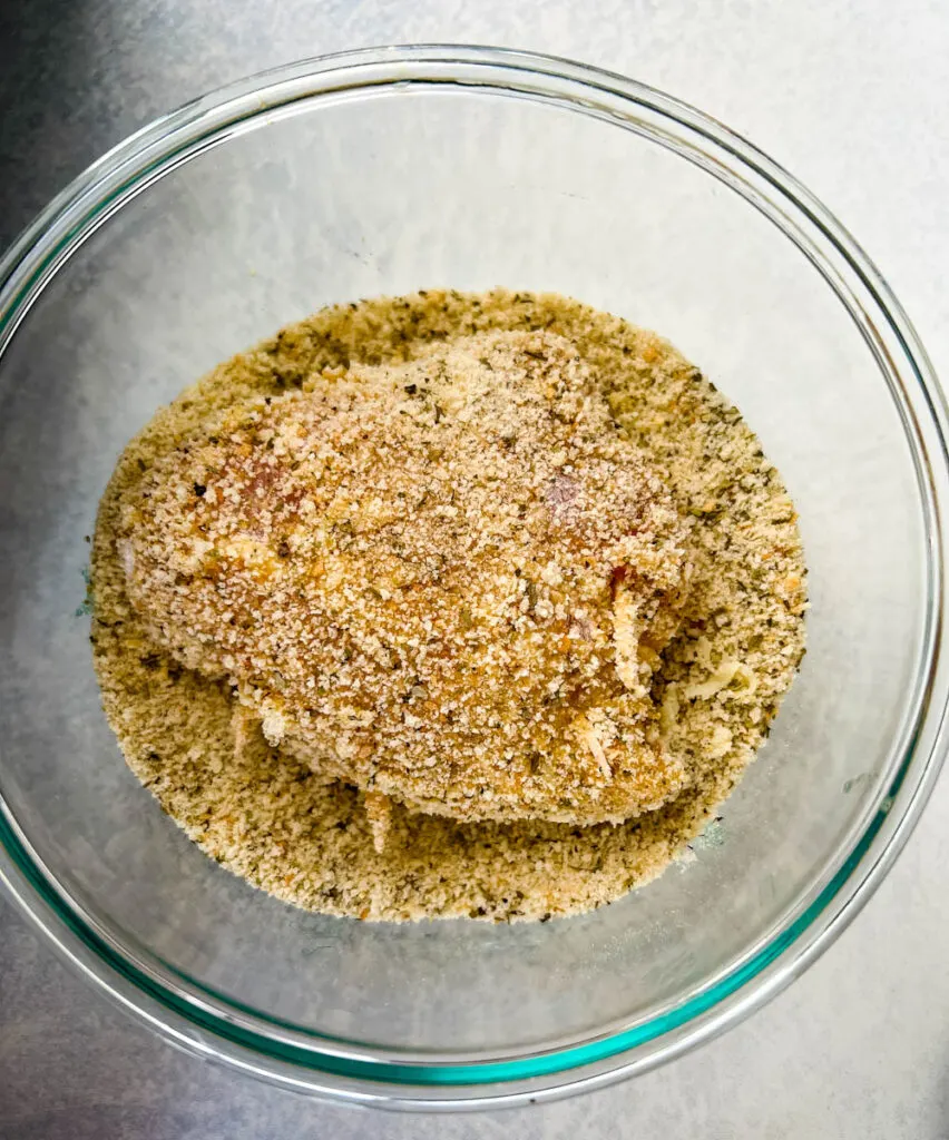 uncooked mozzarella stuffed chicken breast in a glass bowl with breadcrumbs