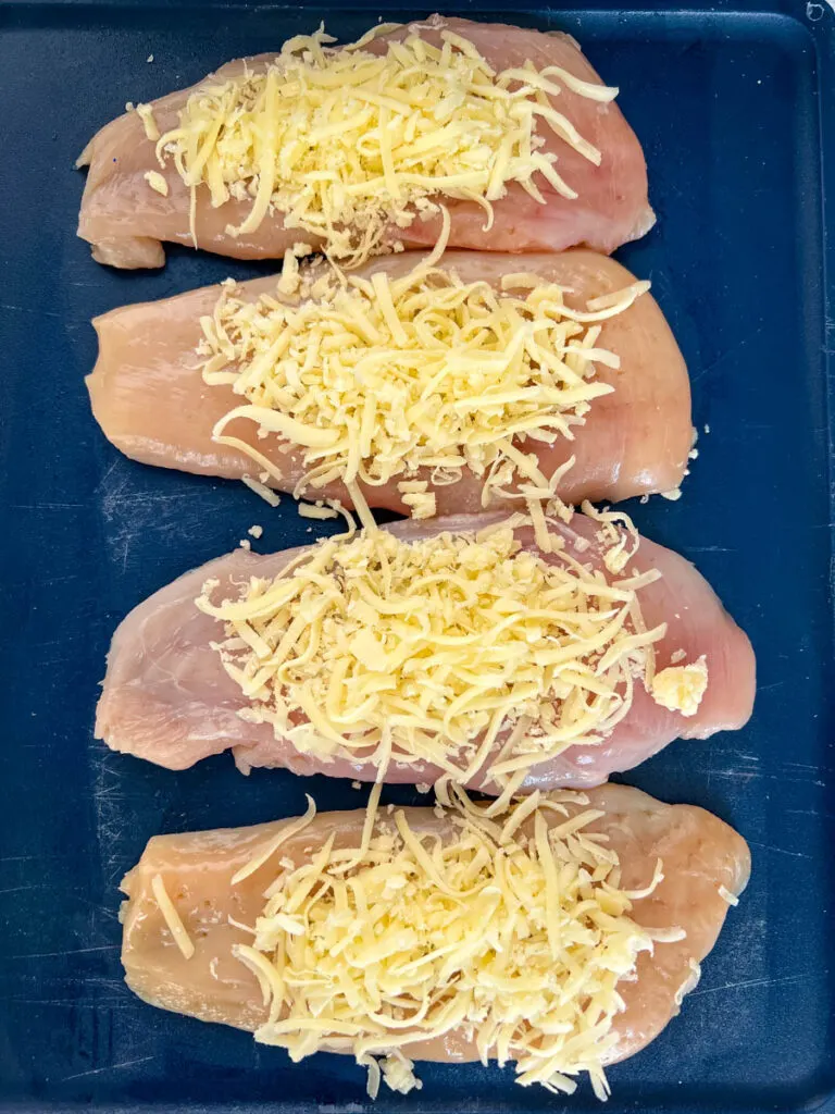 raw chicken breasts on a cutting board topped with mozzarella cheese