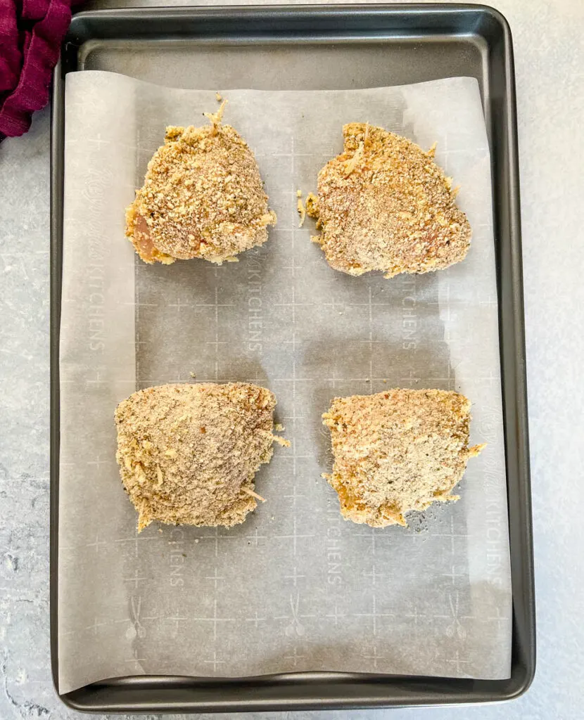 uncooked breaded stuffed mozzarella chicken breast on a sheet pan