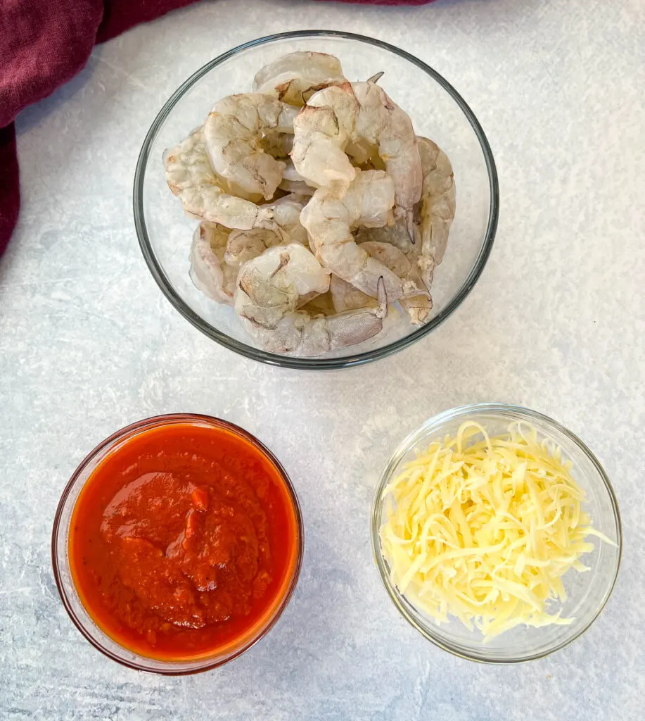 raw shrimp, marinara sauce, and shredded mozzarella in separate glass bowls