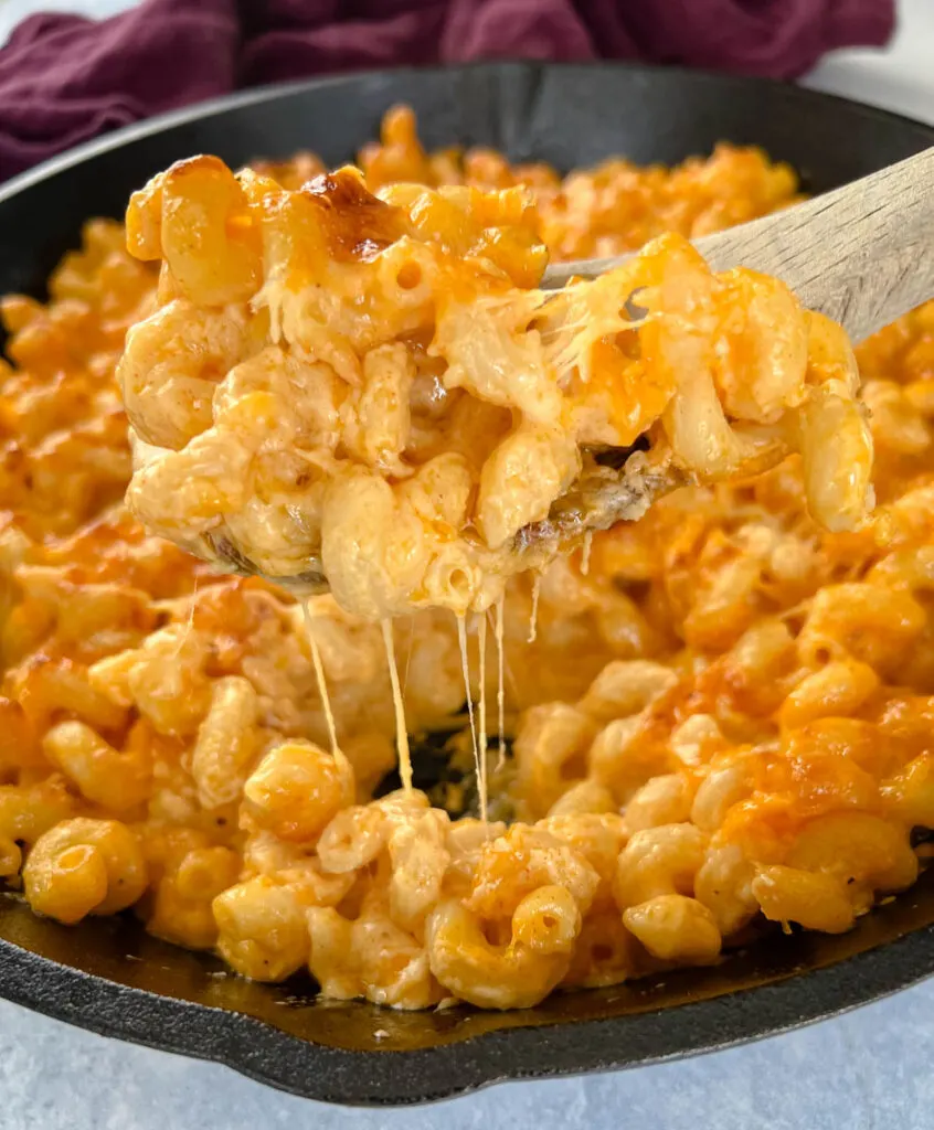 a wooden spoonful of smoked mac and cheese in a cast iron skillet