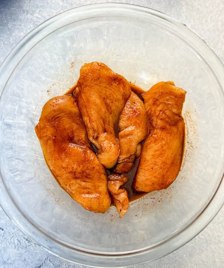 raw chicken breasts in a glass bowl with soy sauce and dry rub