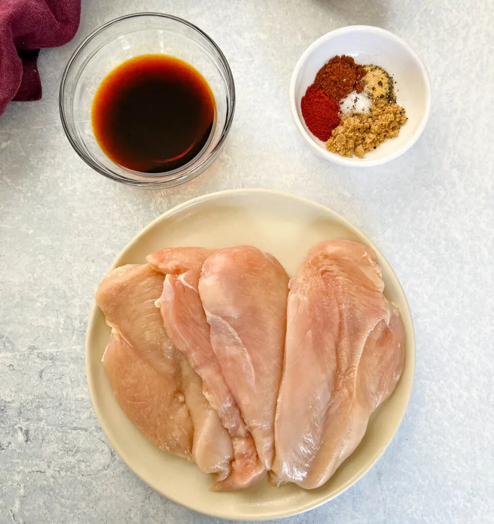 raw chicken breasts on a plate along with 2 bowls of soy sauce and spices