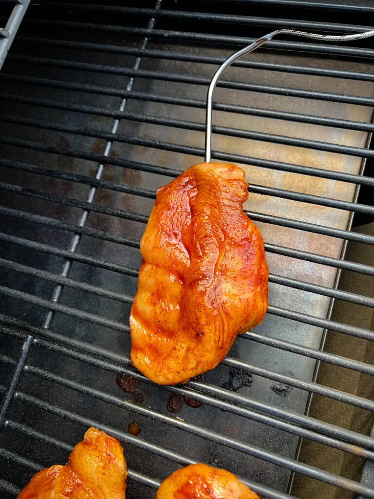 raw chicken breasts on a Traeger smoker grill with a probe