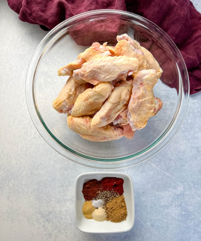 raw chicken wings in a glass bowl and a bowl with dry rub spices