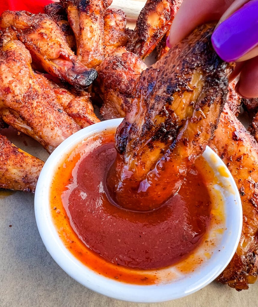 person holding Traeger smoked chicken wings dipped in BBQ sauce
