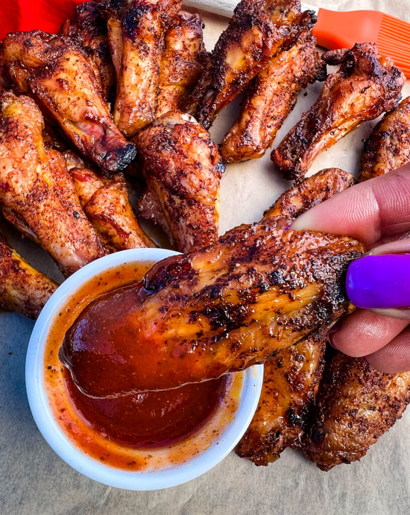 person holding Traeger smoked chicken wings dipped in BBQ sauce
