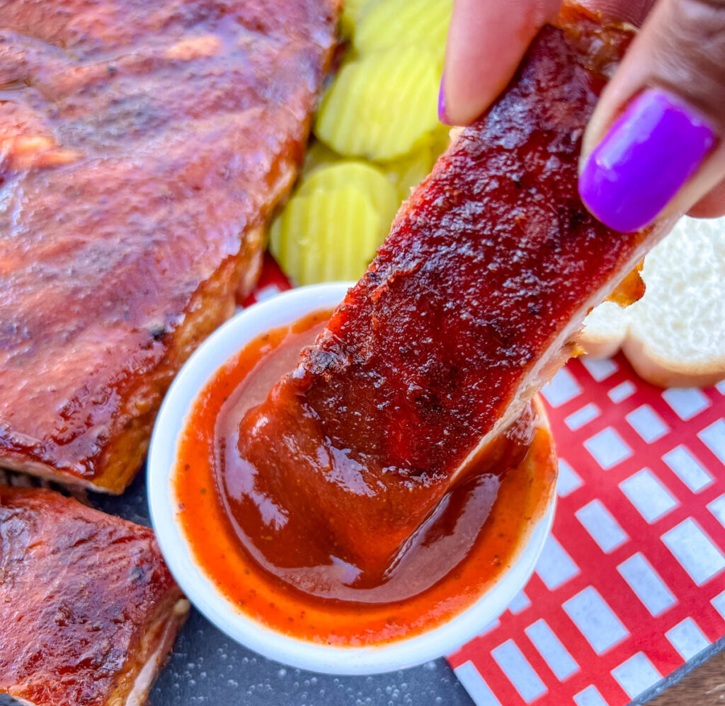 person holding smoked rib dipped in BBQ sauce