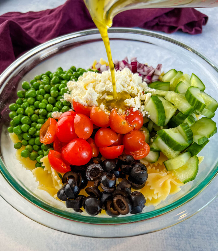Italian dressing poured into bowl of bow tie pasta salad