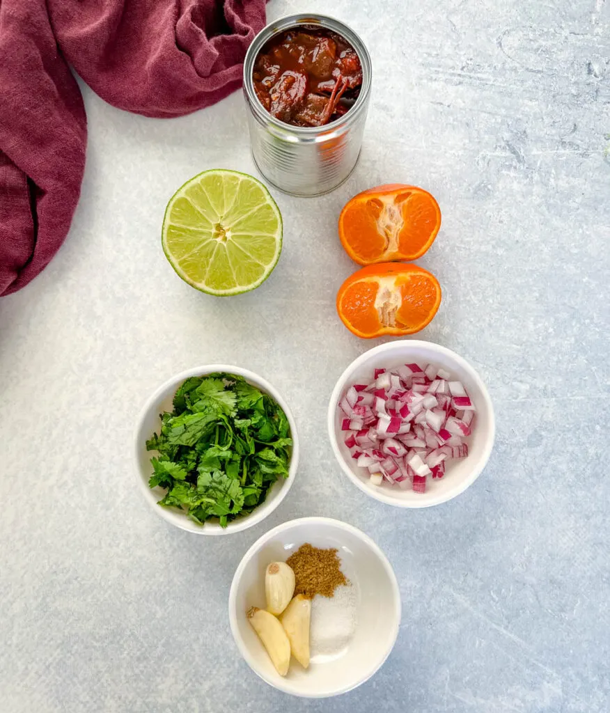 chipotles in adobo sauce, limes, oranges cilantro, onions, and spices on a flat surface