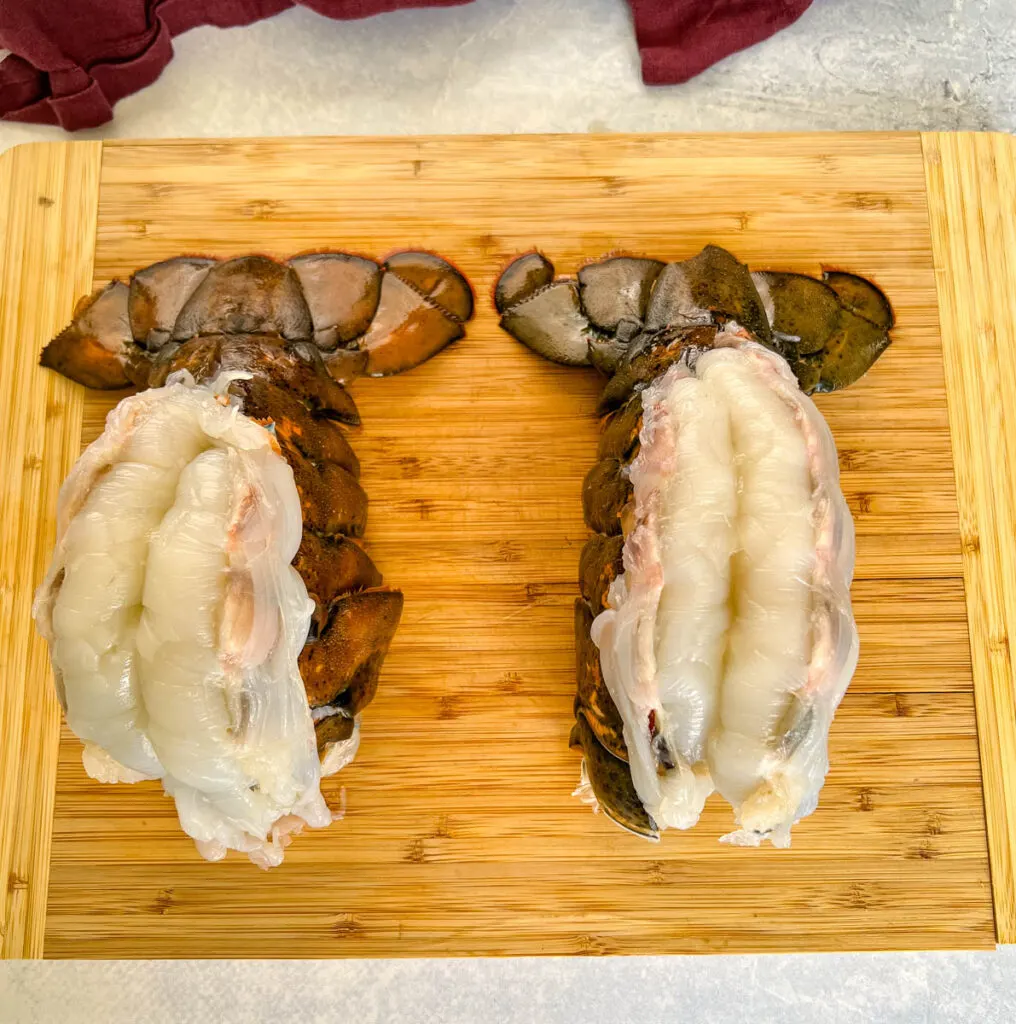 raw butterflied lobster tail on a cutting board