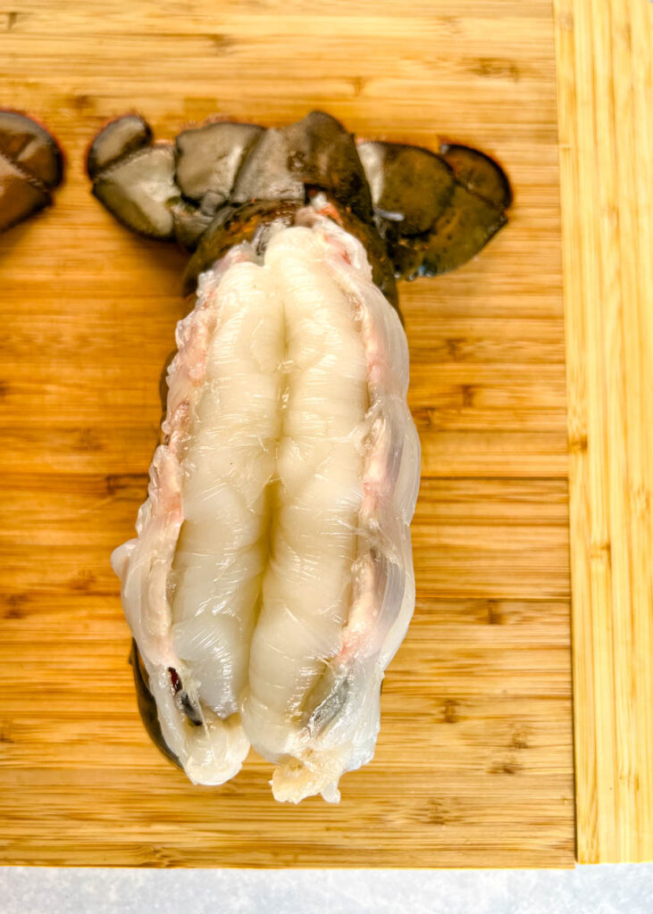 raw butterflied lobster tail on a cutting board