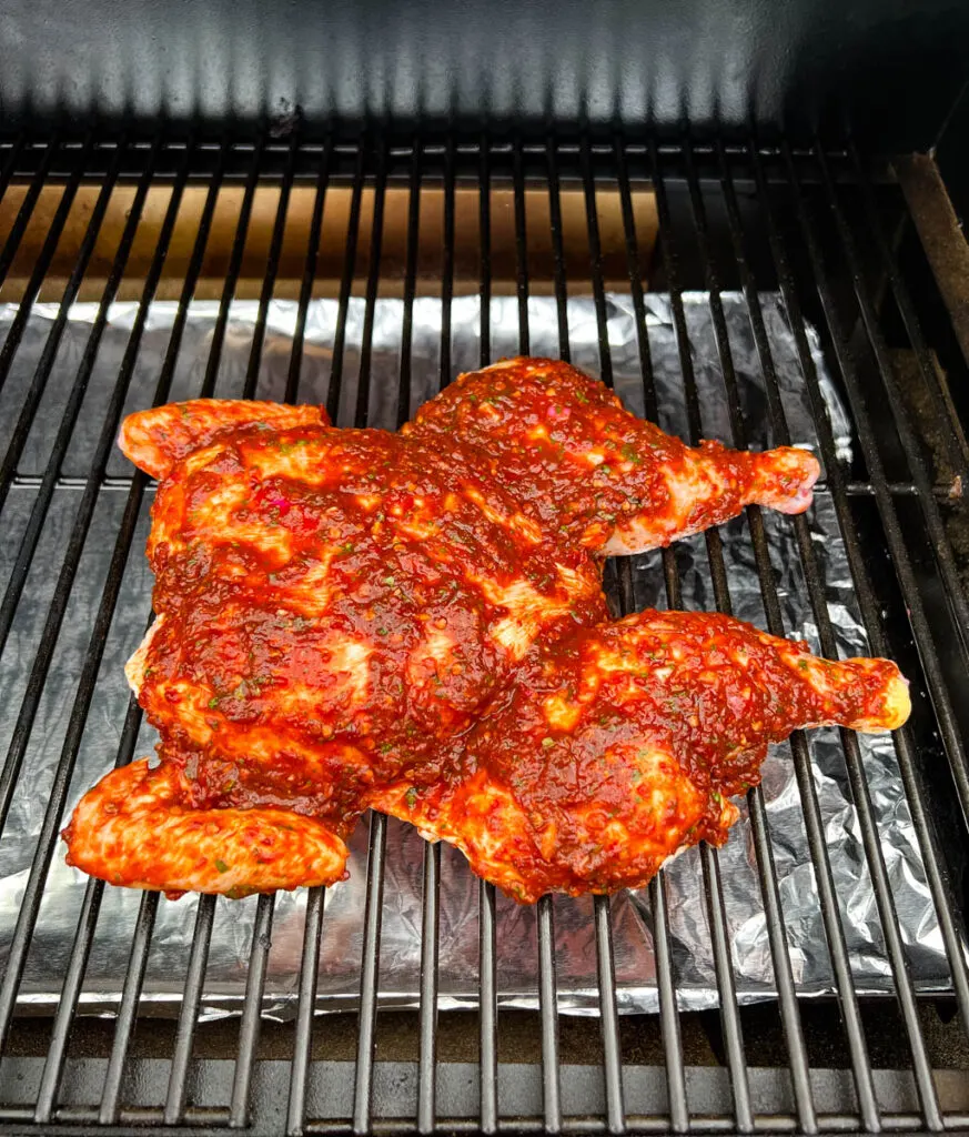 seasoned and raw whole chicken on a Traeger pellet grill smoker