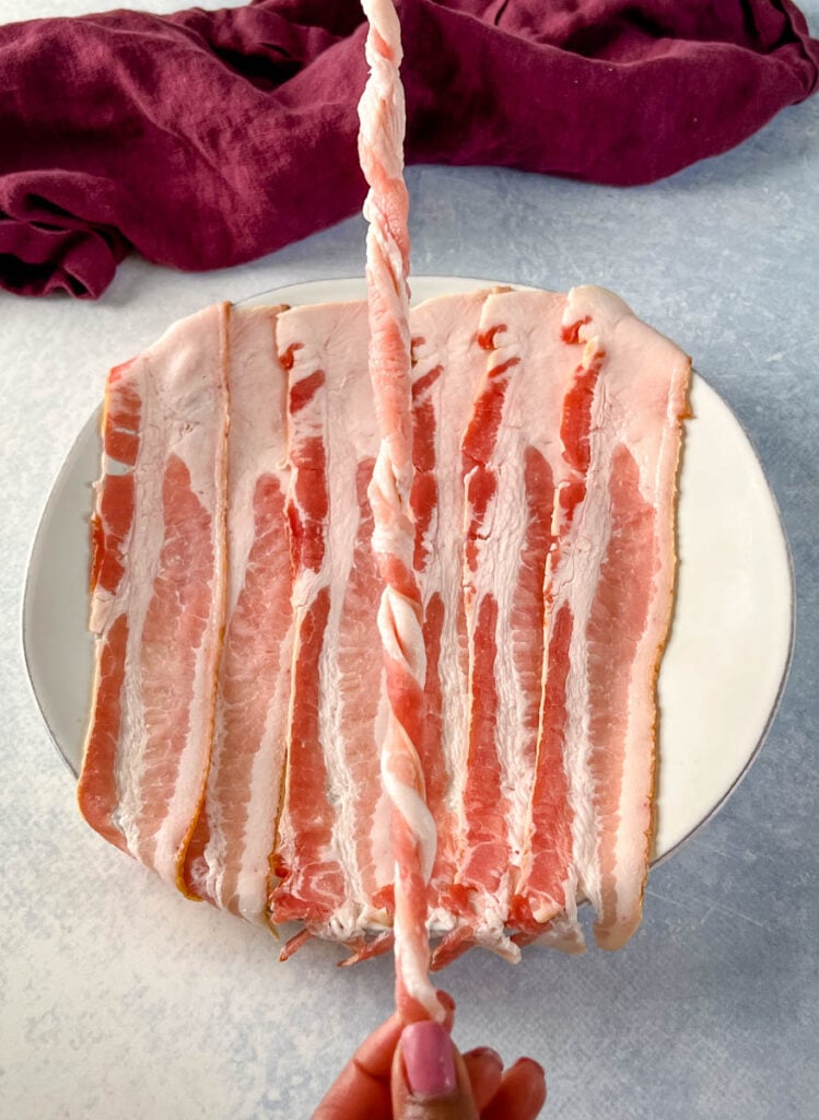 person holding a piece of uncooked twisted bacon