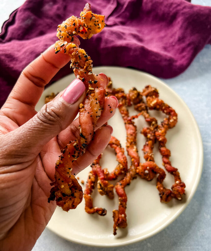 person holding a piece of cooked twisted bacon