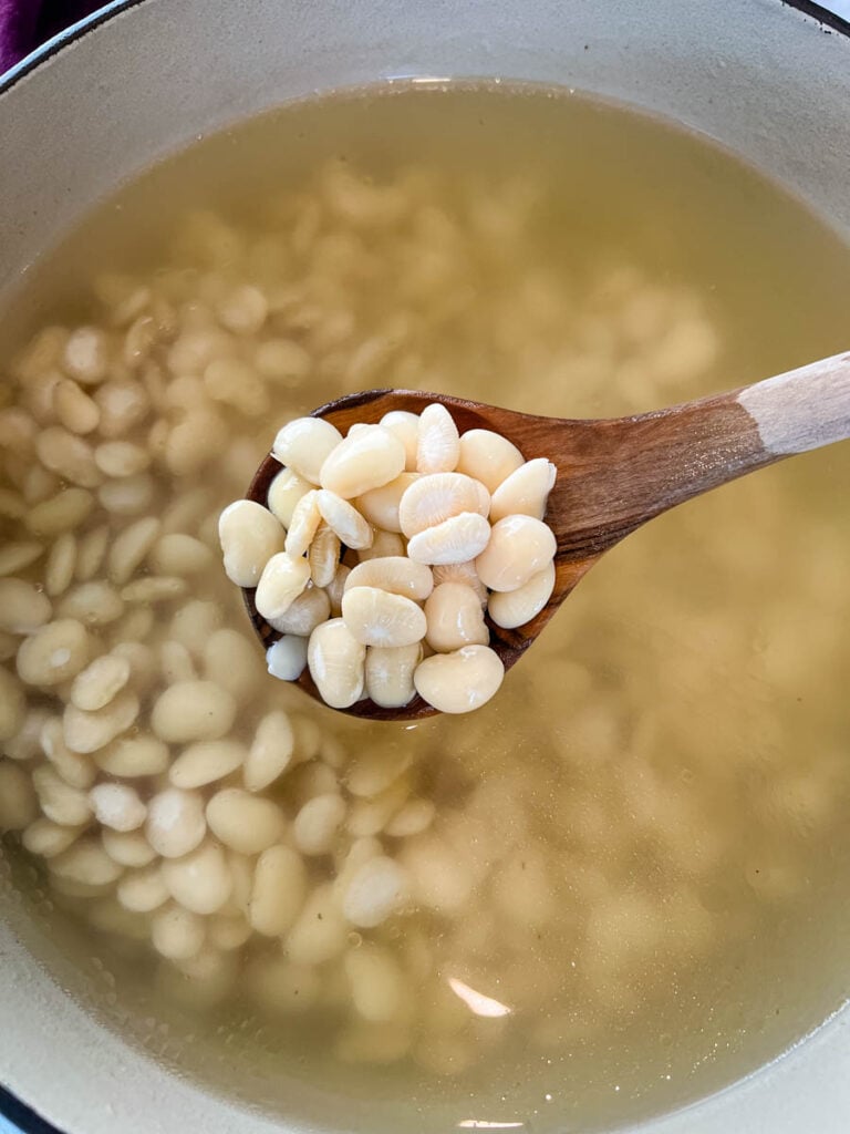 a wooden spoonful of Southern butter lima beans in a Dutch oven