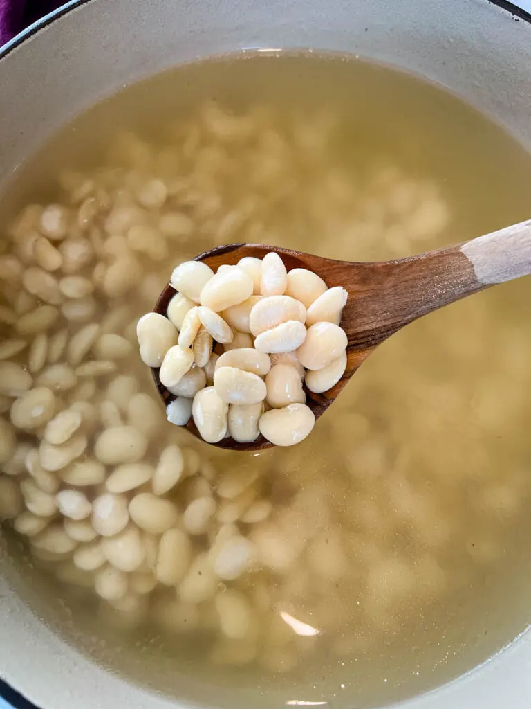 a wooden spoonful of Southern butter lima beans in a Dutch oven