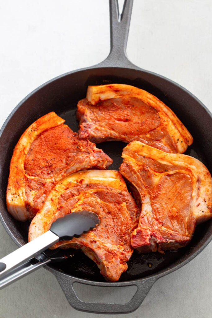 raw seasoned bone in pork chops in a cast iron skillet