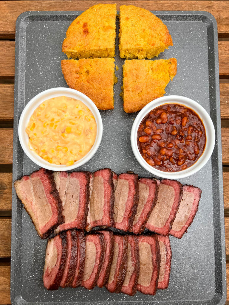 Traeger smoked brisket on a plate with baked beans and cornbread