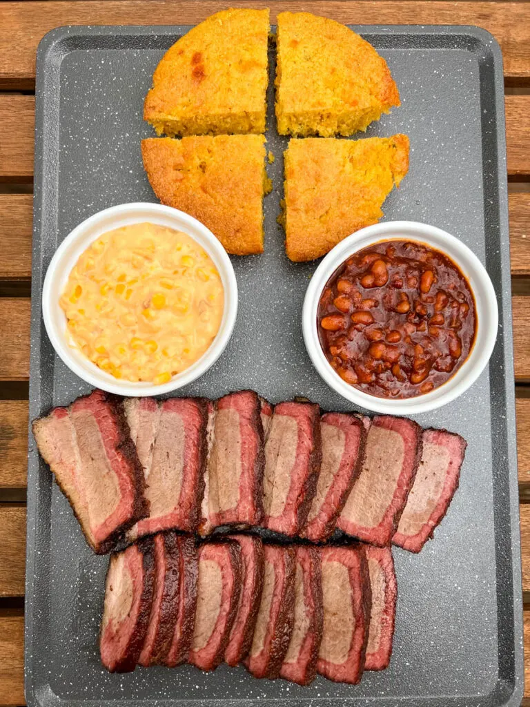 Traeger smoked brisket on a plate with baked beans and cornbread