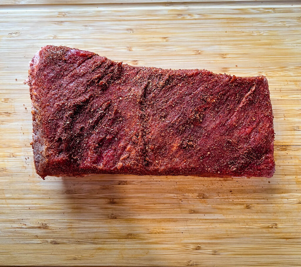 raw seasoned brisket on a bamboo cutting board