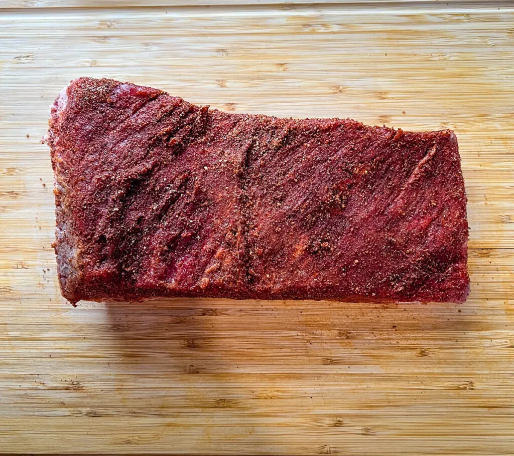 raw seasoned brisket on a bamboo cutting board