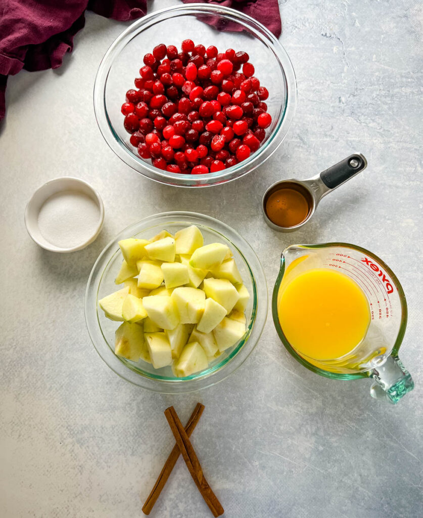 cranberries, sliced apples, cinnamon sticks, sugar, honey, and orange juice in separate bowls
