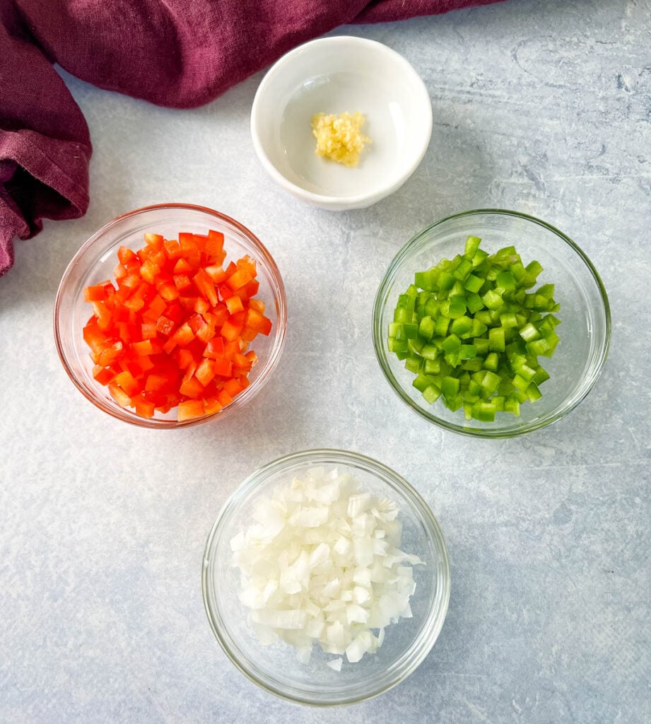 red peppers, green peppers, onions, and garlic in separate bowls