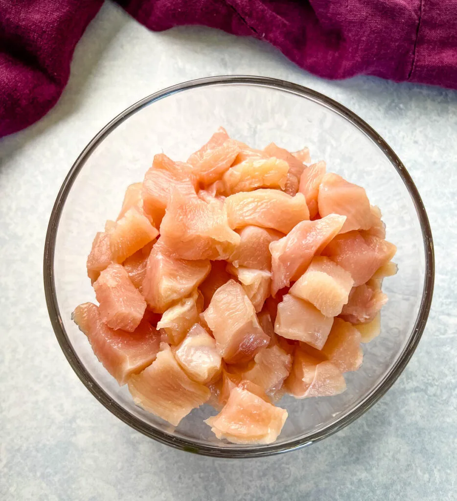 raw and cubed chicken breasts in a glass bowl