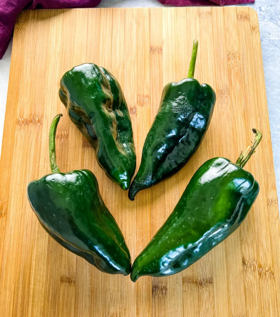 4 poblano peppers on a wood cutting board