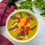 roasted creamy poblano pepper soup in a white bowl with shredded cheese and tortilla strips