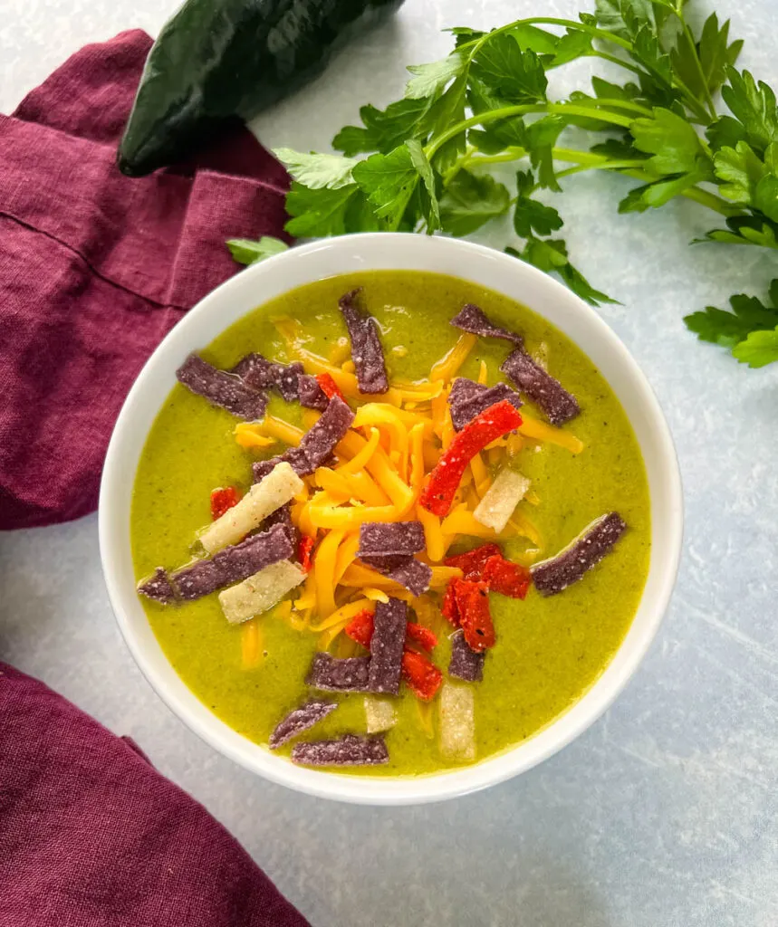 roasted creamy poblano pepper soup in a white bowl with shredded cheese and tortilla strips