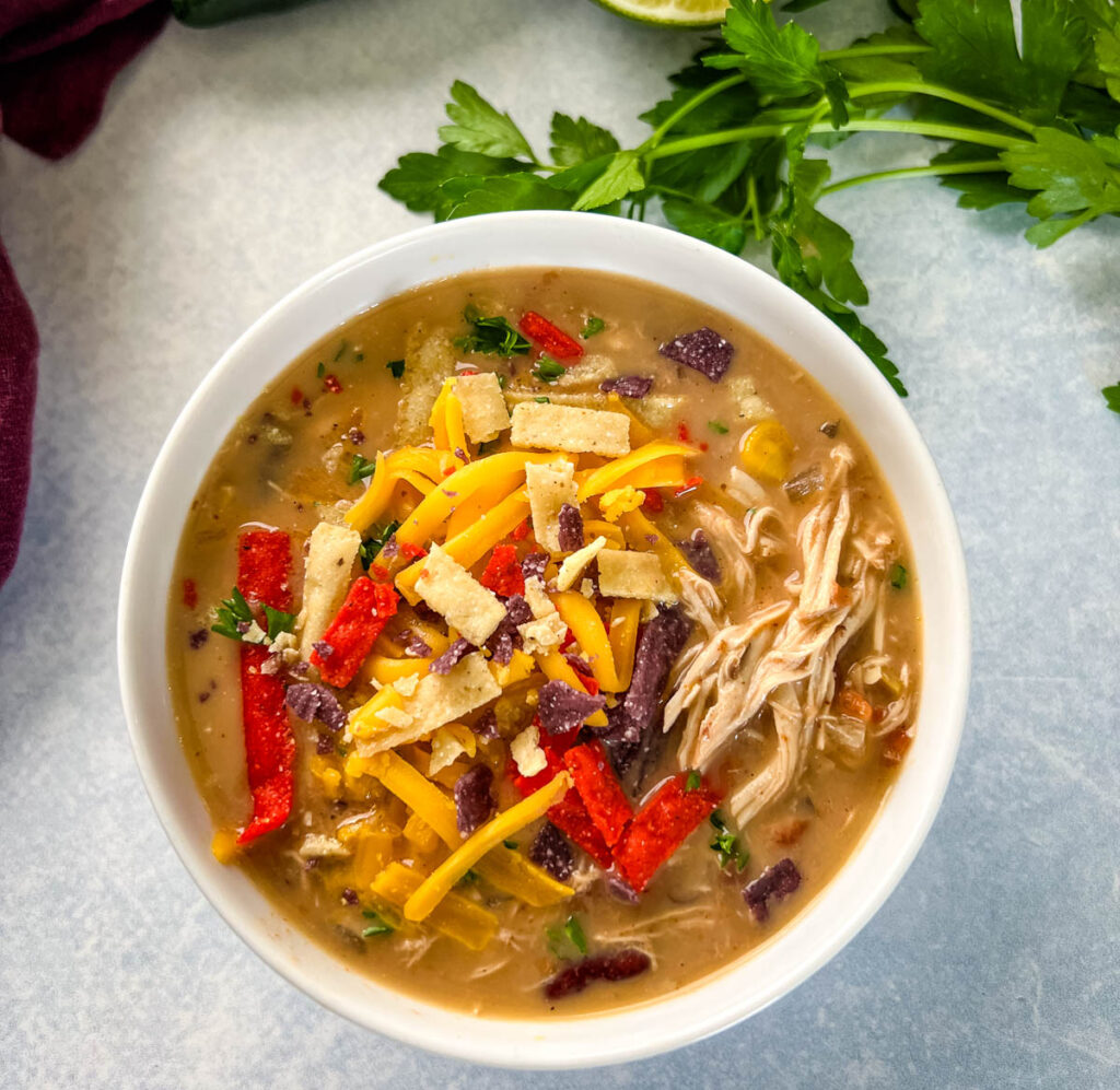 slow cooker chicken taco soup in a white bowl with tortilla strips and cheese