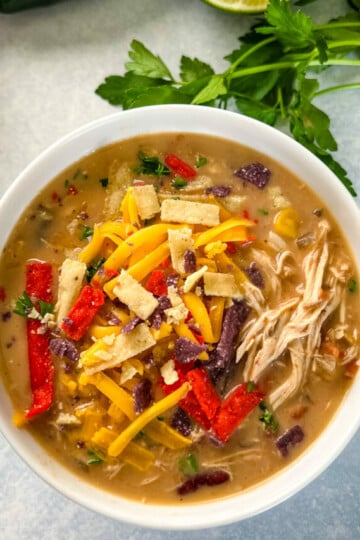 slow cooker chicken taco soup in a white bowl with tortilla strips and cheese