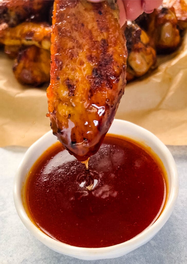 person holding honey hot wing with hot sauce