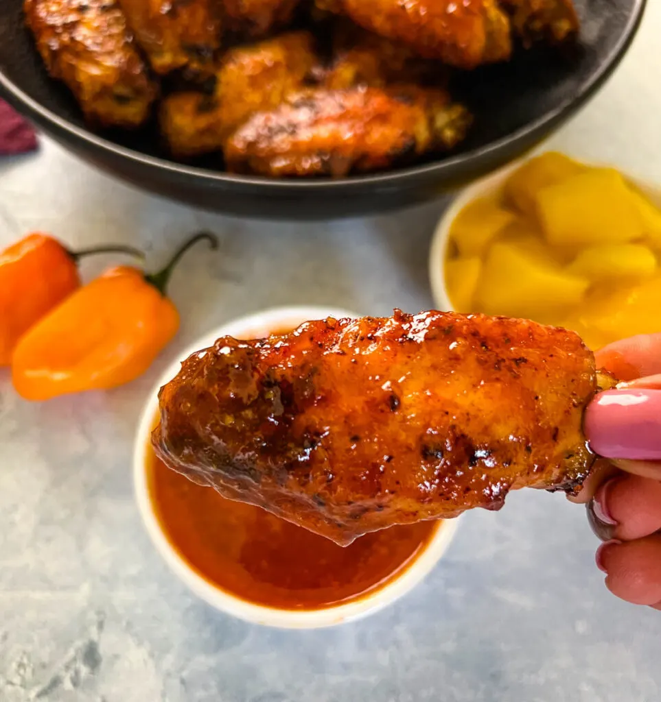 person holding mango habanero wing dipped in sauce