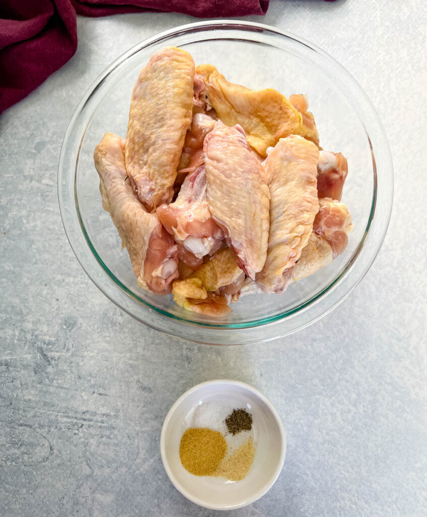 raw chicken wings in a glass bowl with a bowl of spices