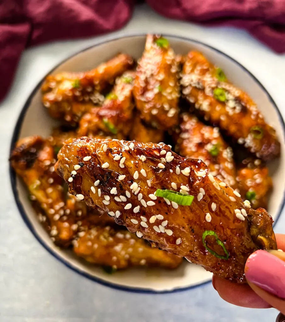 person holding teriyaki chicken wing with sesame seeds
