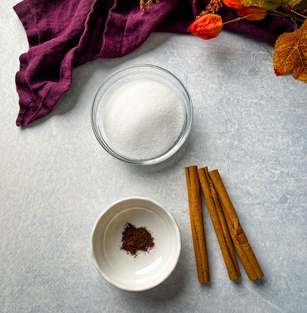 sweetener, spices, and cinnamon sticks in separate glass bowls