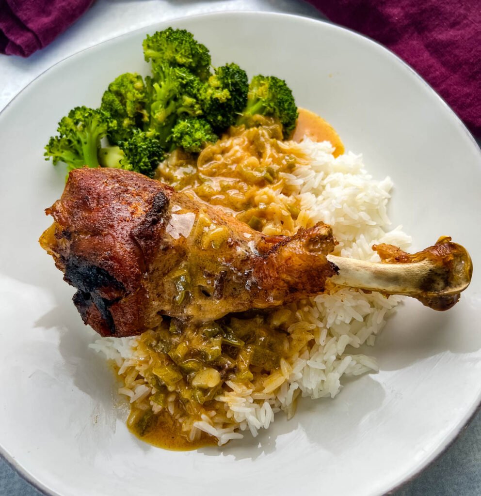 baked turkey leg on a plate with rice, gravy, and broccoli