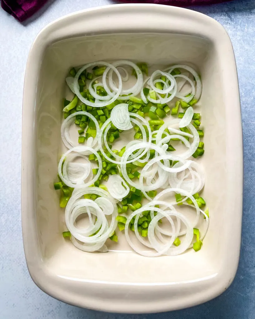chopped green peppers and onions in the bottom of a baking dish