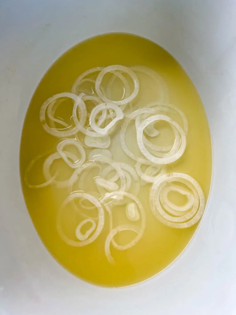 sliced onions and broth in a Crockpot slow cooker