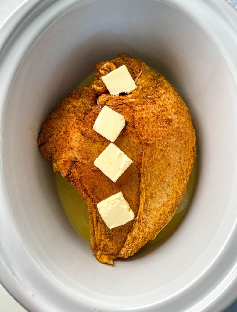 raw seasoned bone-in turkey breast in a Crockpot slow cooker with butter