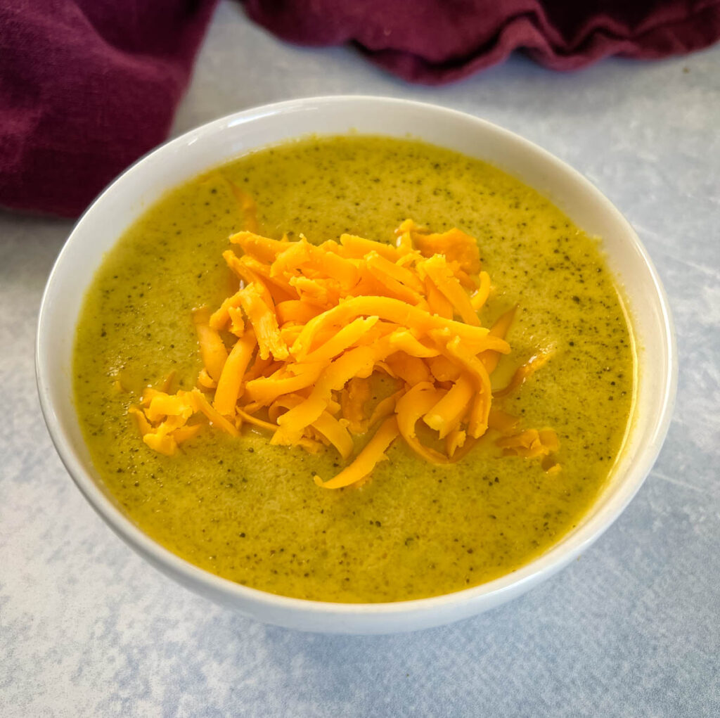 slow cooker Crockpot broccoli cheese soup in a white bowl with shredded cheese