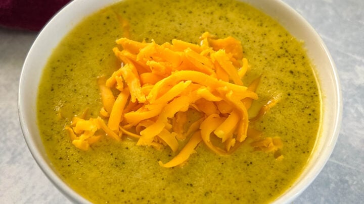 slow cooker Crockpot broccoli cheese soup in a white bowl with shredded cheese