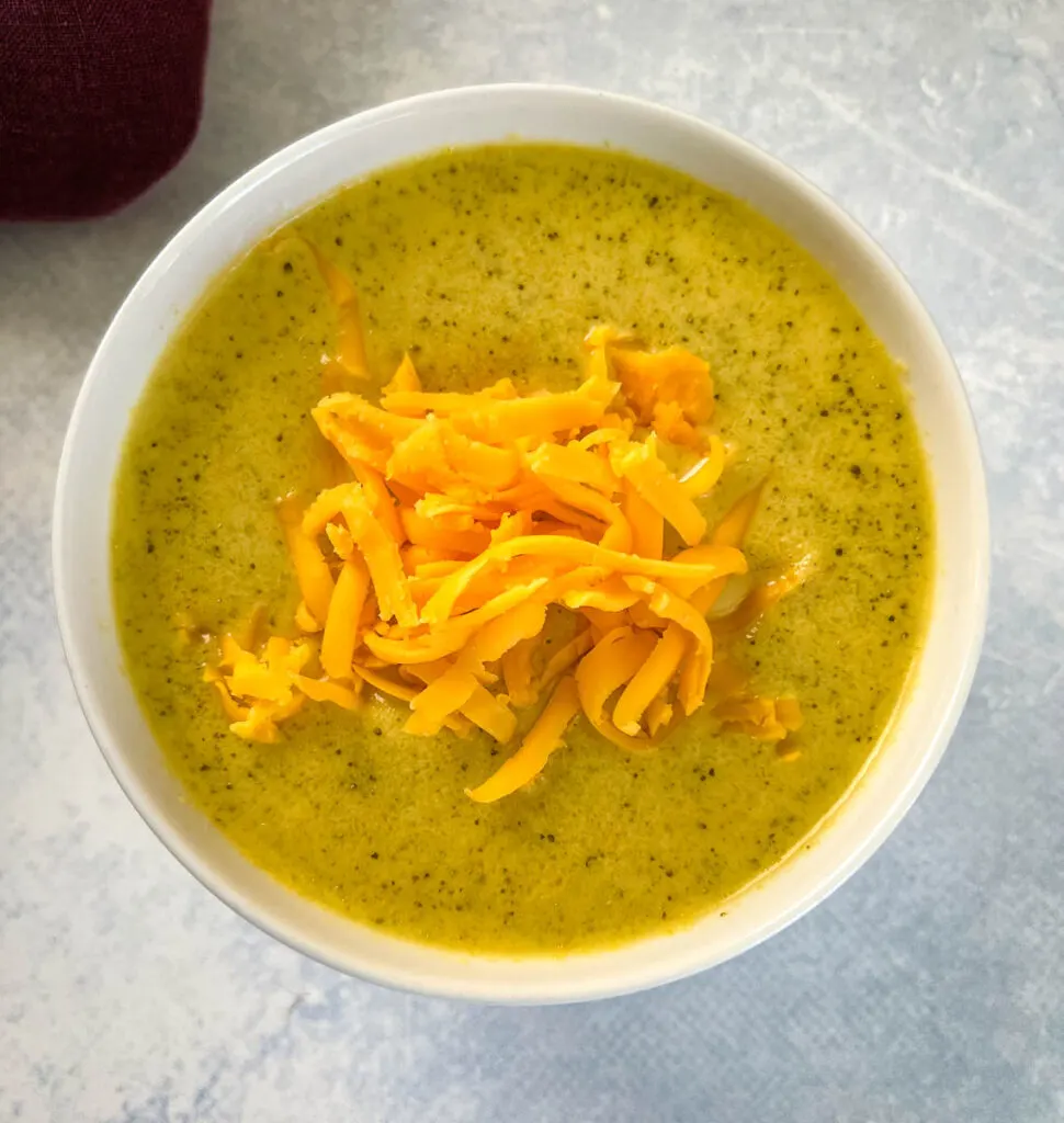 slow cooker Crockpot broccoli cheese soup in a white bowl with shredded cheese