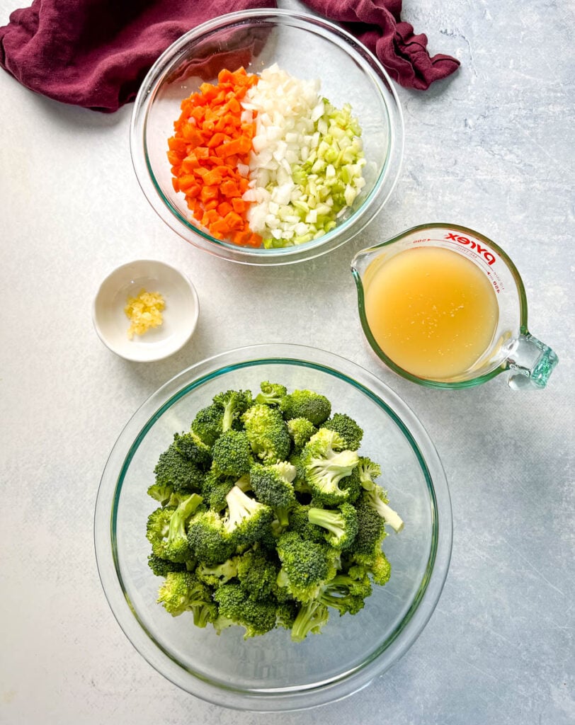 fresh broccoli, carrots, onions, celery, broth, and garlic in separate bowls