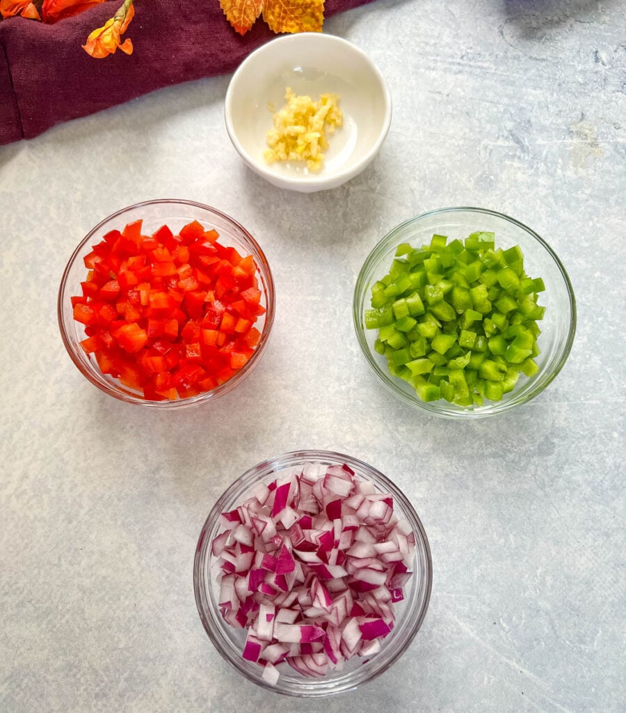 garlic, green peppers, red peppers, and red onions chopped in separate glass bowls