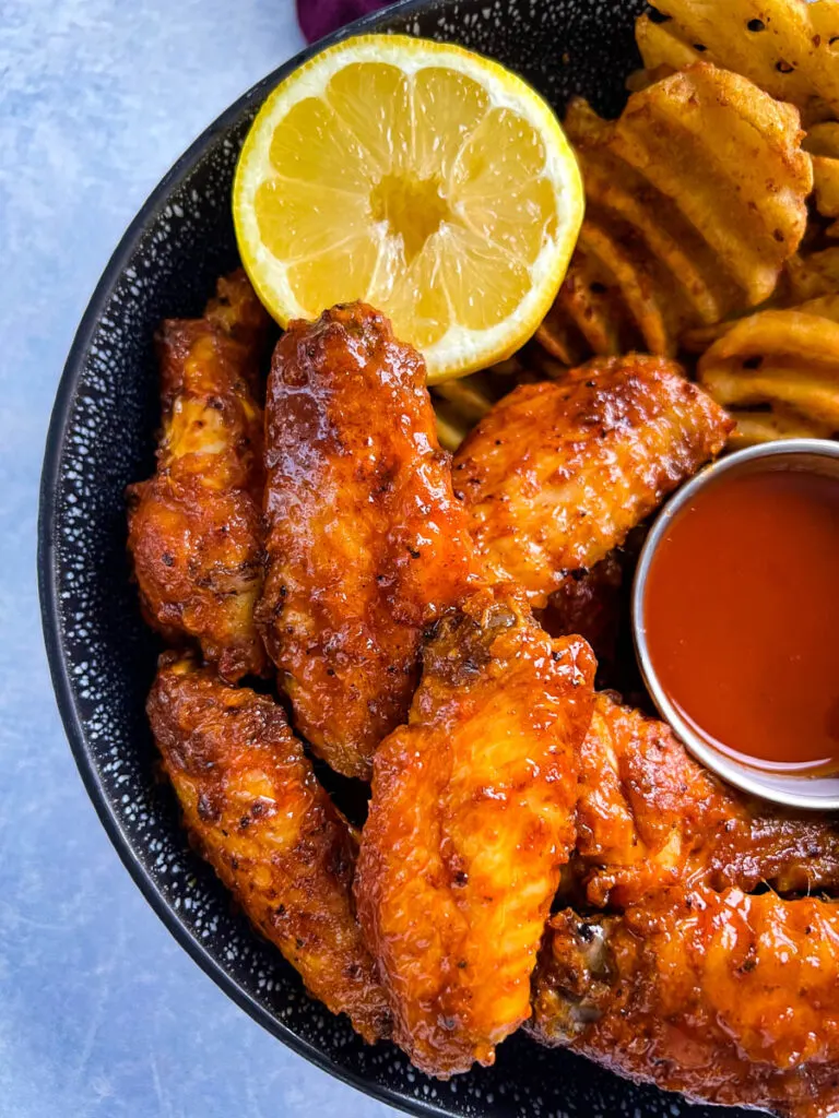 hot lemon pepper chicken wings in a black bowl with fresh lemon and hot sauce