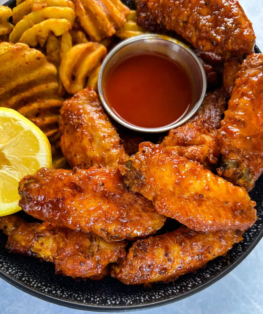 hot lemon pepper chicken wings in a black bowl with fresh lemon and hot sauce